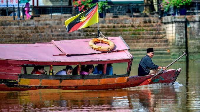 Barca de pasajeros navegando por un río de Sarawak con la bandera de Malasia